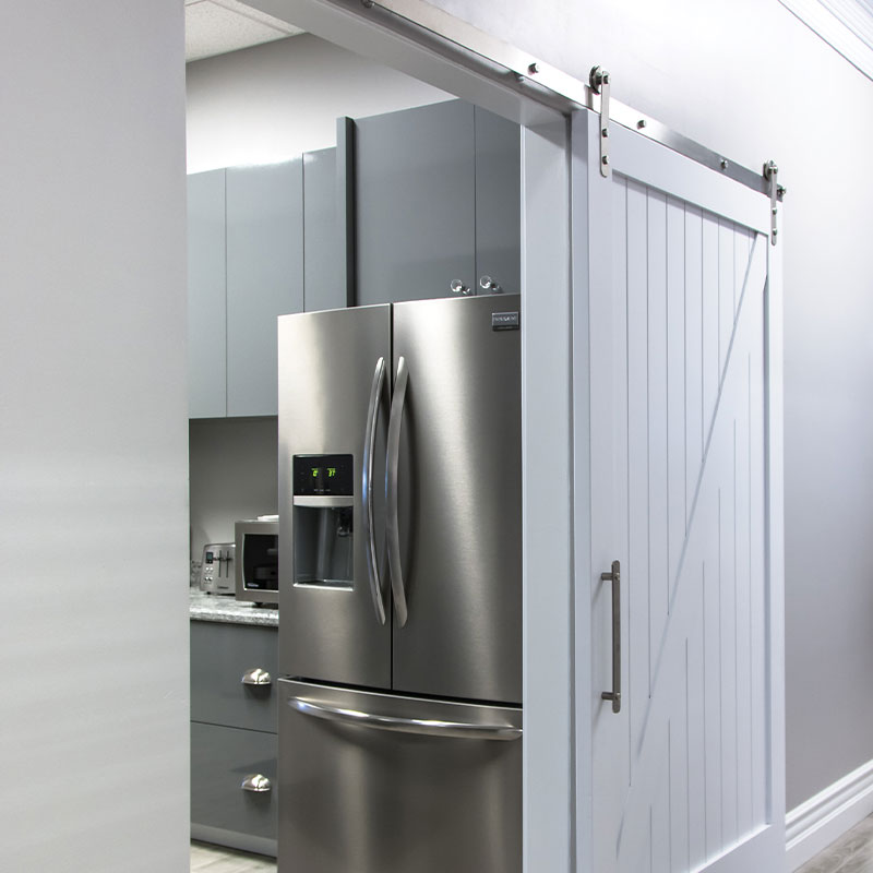 Modern Farmhouse style Kitchen with a stainless steel refrigerator and white barn door with stainless steel track and hardware
