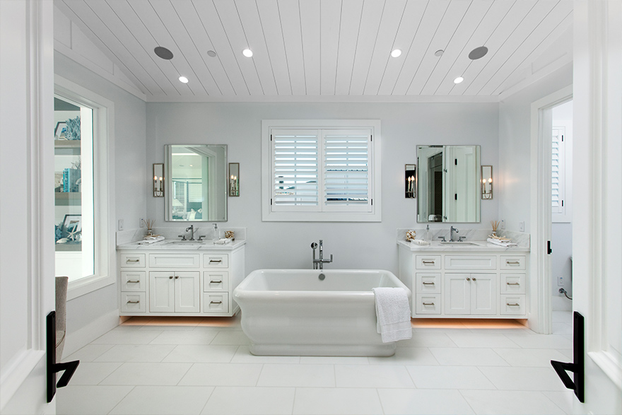 White bathroom with 2 matching vanity sinks on the left and right and a white tub in the middle with a white shiplap accent ceiling