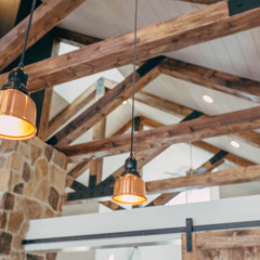 Tilted up view of a pointed ceiling with exposed triangle shaped polyurethane wood grain beams and hanging copper lights