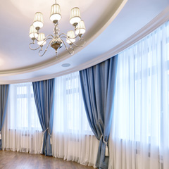 Traditional luxury style curved window wall using ValuFlex crown moulding with sheer white drapes and tied up light blue opaque drapes and a 7 light chandelier