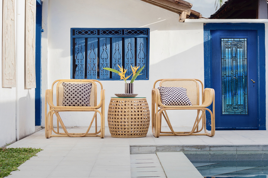 Mediterranean style home with 2 bamboo beach chairs with a round woven bamboo mini table between them next to a pool on the right and a blue full lite Belville door