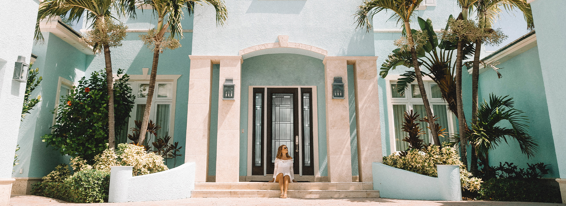 A woman in white dress is sitting at the front steps of a Mediterranean style home with a full light Bellville door with sidelites