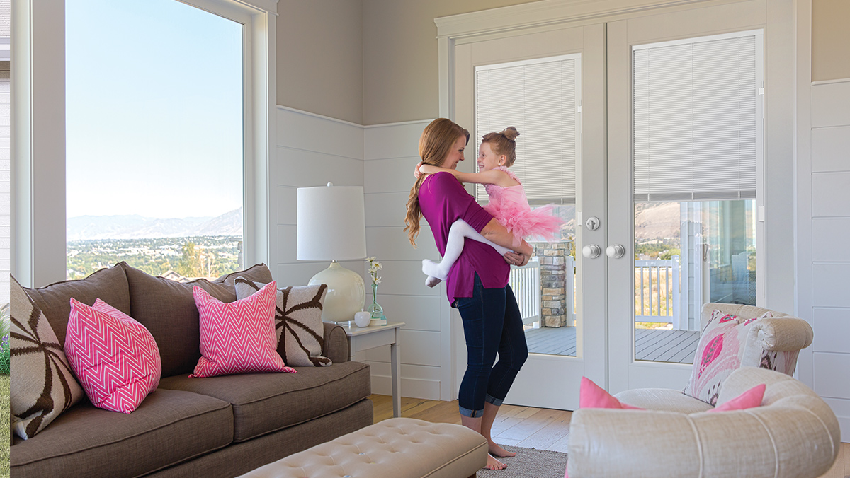 A mom holding her young daughter in a pink ballerina outfit in a living room in front of VistaGrande double doors with built in mini blinds