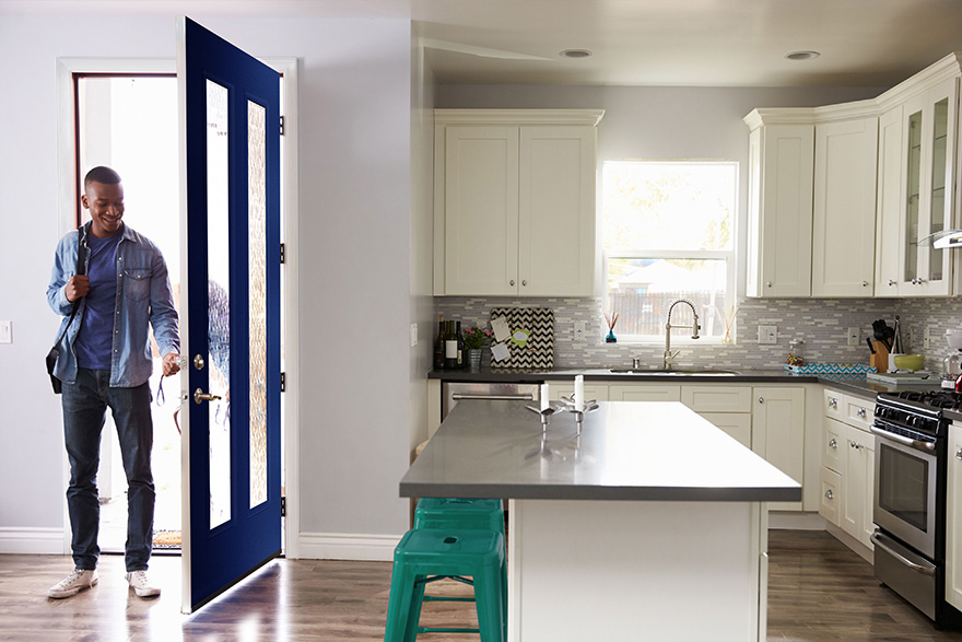 A man is coming into his modern home kitchen with a navy blue 2 vertical lite front door