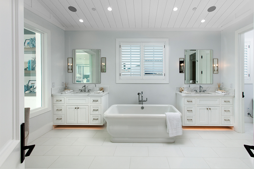 Coastal style bathroom with white moulding and double vanity sinks with a tub and window in between