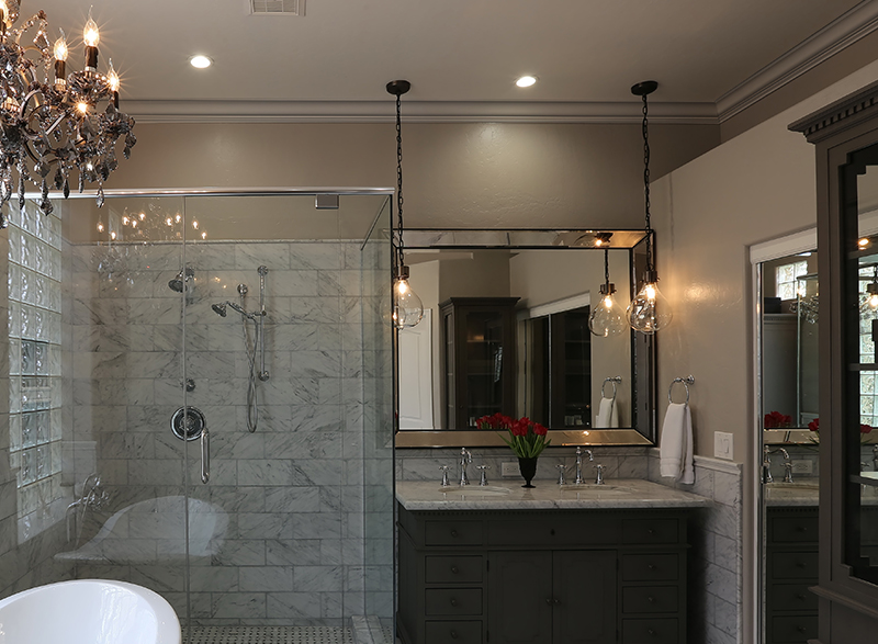 Colonial Revival style bathroom with marble backsplash and white crown moulding, clear glass shower to the left, white tub in front of shower, and double sink vanity to the right