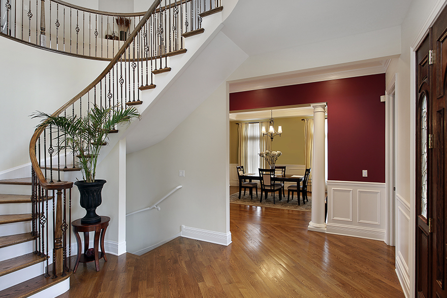 Colonial Revival style home entryway with different types of white moulding, 2 sets of stairs going up and downstairs to the left, forward view of the dining room, and entry door to the right 