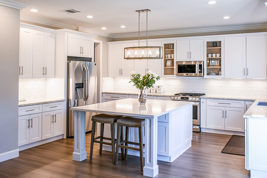 Craftsman style kitchen with grey walls, white crown moulding, white cabinets and drawers, white marble counter tops, stainless steel appliances, and a center island with 2 brown square stools tucked under