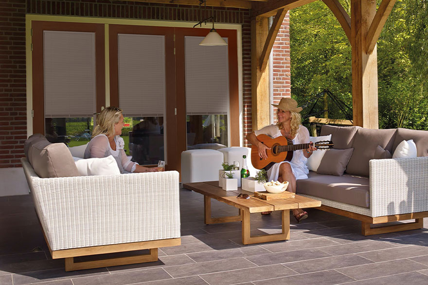 Modern Cottage style back patio with 2 women sitting on 2 different sofas facing each other while the one of the left is holding an acoustic guitar and the women on the right is holding a glass in her hand