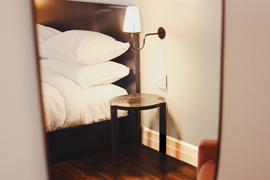 Mirror view of a front corner of side of a bed with a lamp and night stand to its right